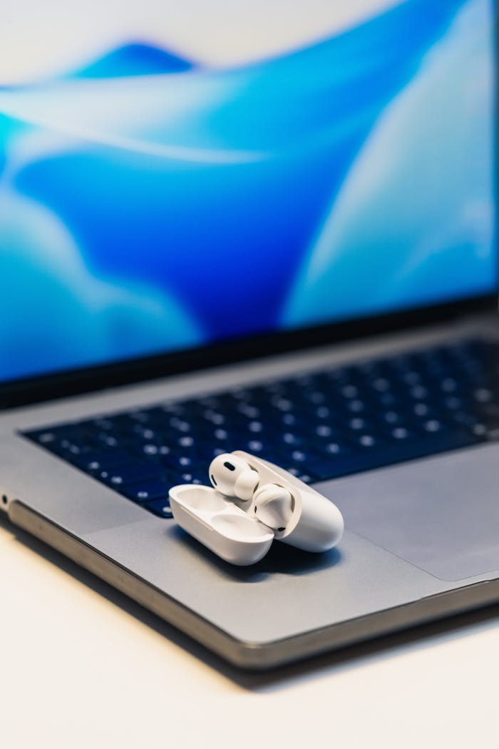 White wireless earbuds resting on a laptop with a vibrant blue screen background.