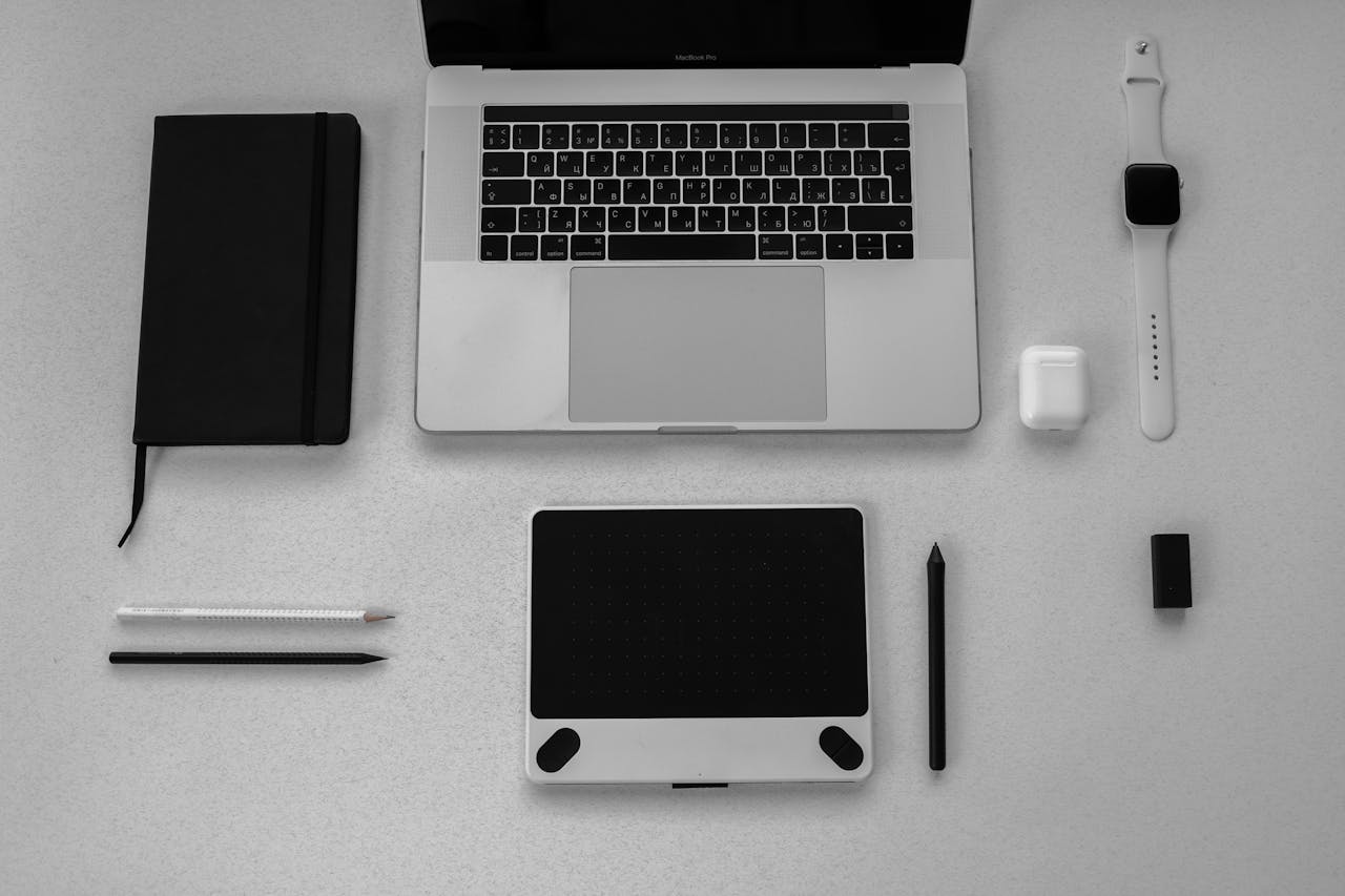 Black and white flatlay of stylish tech gadgets including laptop and smartwatch on a desk.